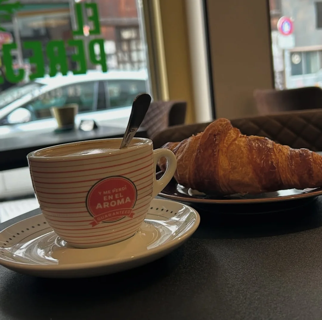 Café y croissant sobre una mesa junto al ventanal.