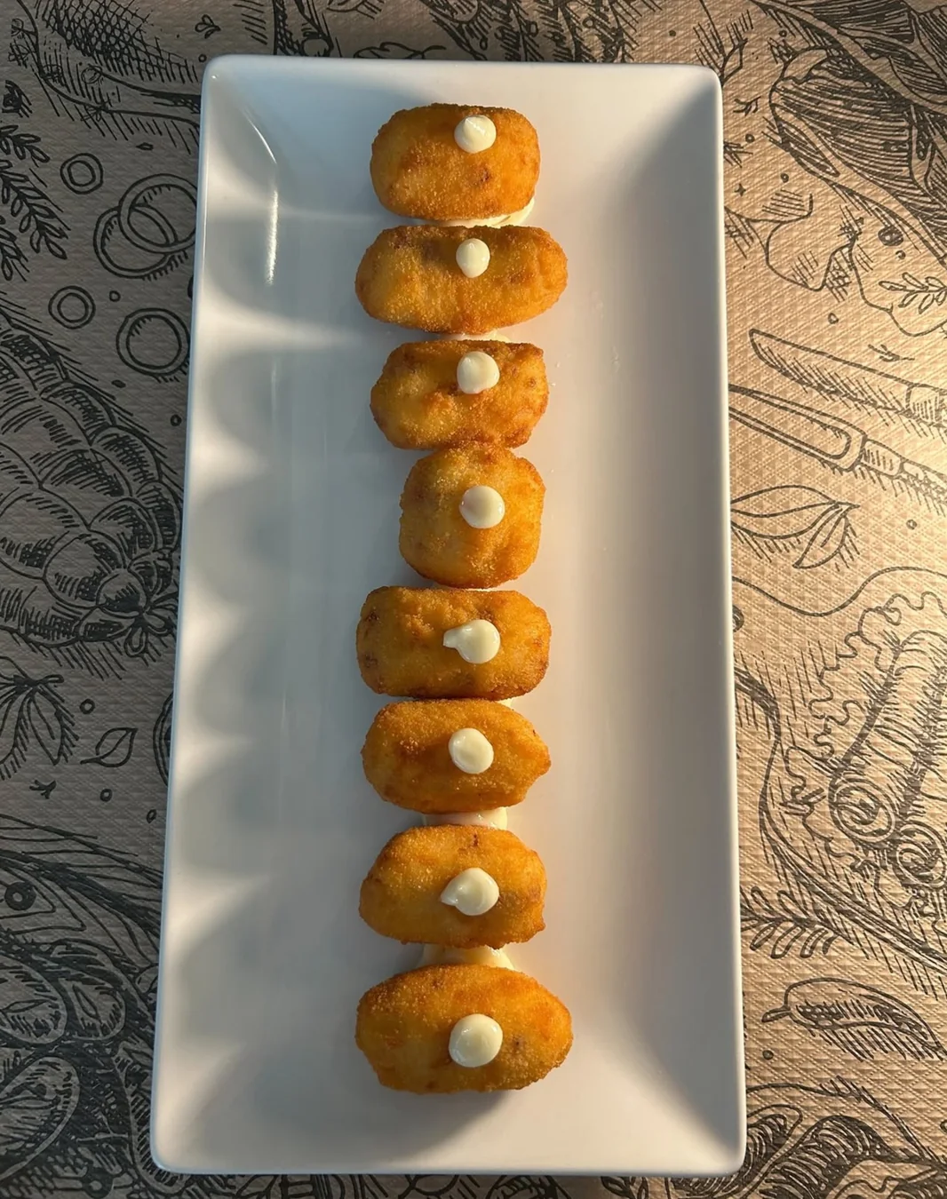 Una fuente de croquetas doradas con pequeños toques de salsa.