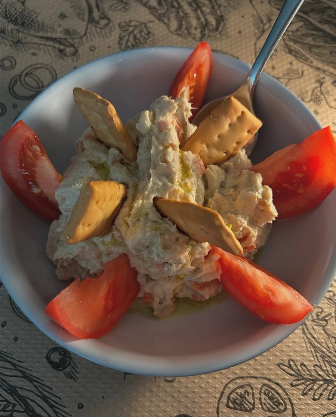 Una ensaladilla acompañada de tomate y pequeños picos crujientes.